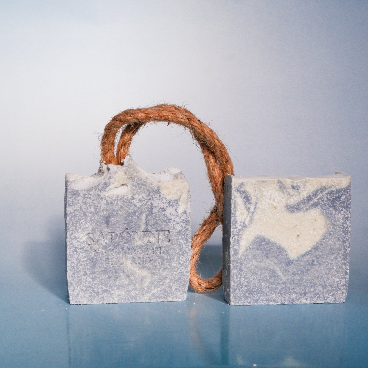 Two rectangular soap bars with a rope handle on a light blue background