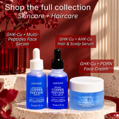 Three Sapônne skincare products displayed together: a blue serum bottle with a white dropper cap, a blue hair & scalp serum bottle with a black dropper cap, and a blue face cream jar with a white lid. The products are arranged on a stone pedestal with promotional text overlays and a warm red background.