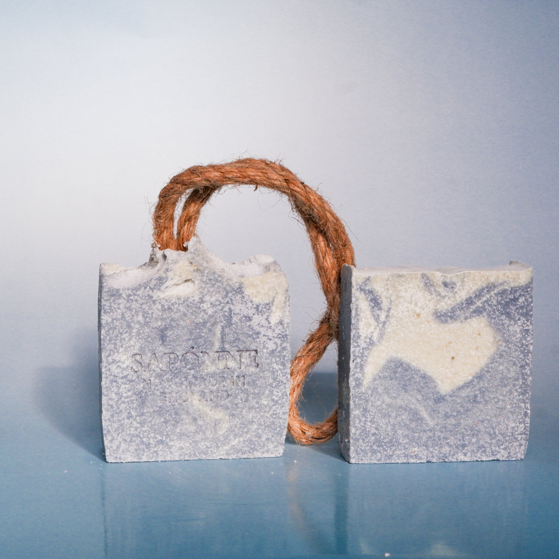 Two rectangular soap bars with a rope handle on a light blue background